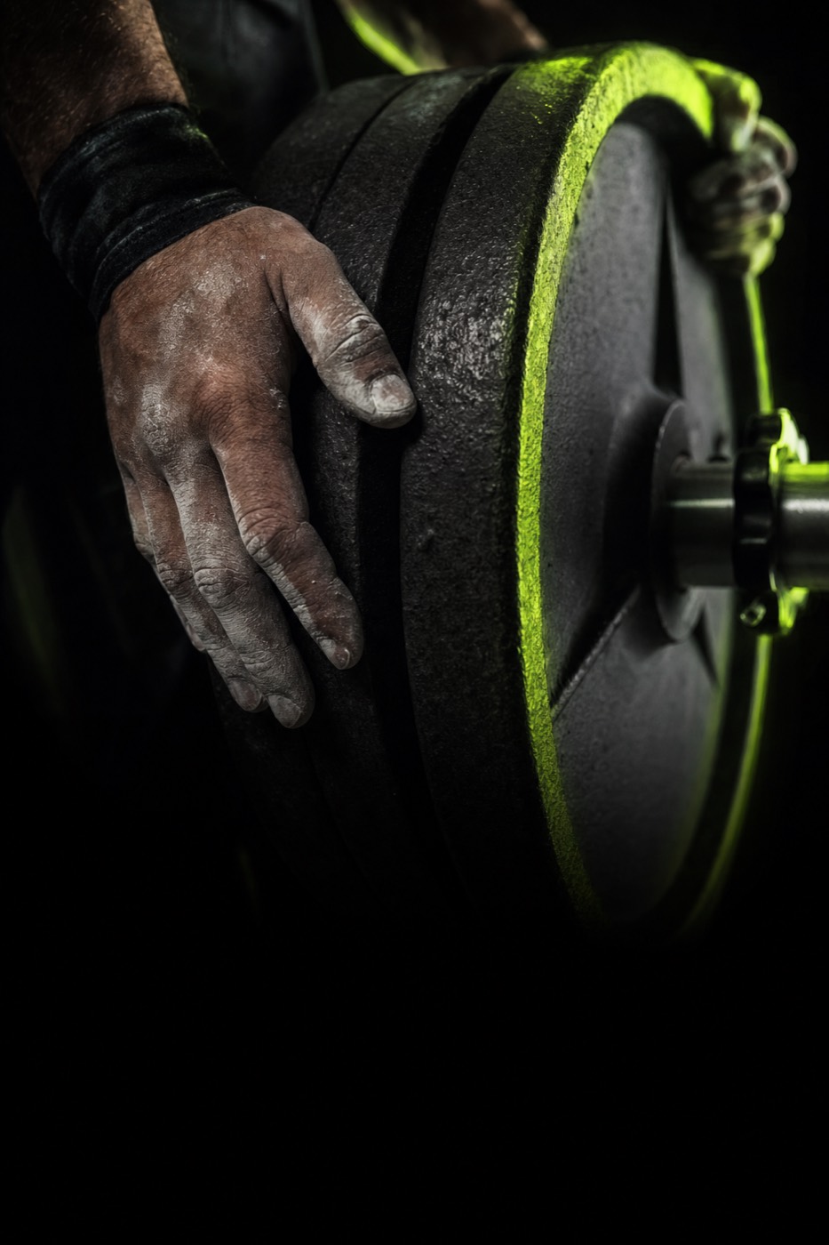A chalked hand loading a plate onto a barbell, lit with a volt-green rim
